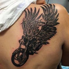 the back of a man's shoulder with a motorcycle and wings tattoo on it