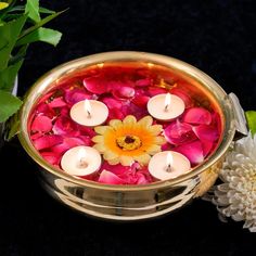 a bowl filled with water and lit candles on top of a table next to flowers