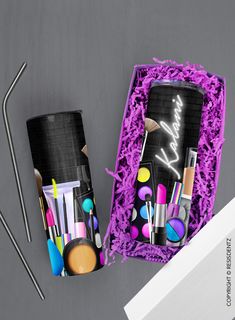 two black containers with makeup and brushes in them