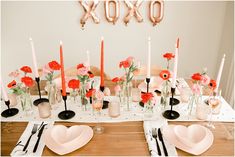 the table is set with pink and red flowers in vases, candles, and plates