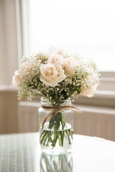 a vase filled with white flowers sitting on top of a table next to a window