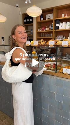 a woman standing in front of a counter holding a white bag and smiling at the camera