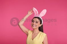 a woman in yellow shirt and bunny ears holding up her hand to the side with pink background