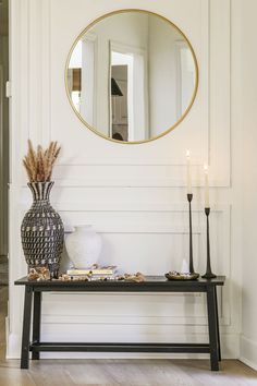 a table with two candles and a vase on it in front of a white wall