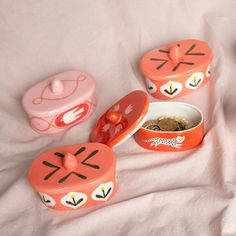 three small tins with designs on them are sitting on a white sheet next to some coins