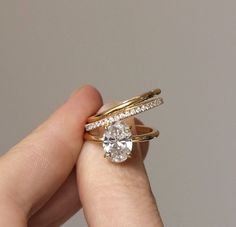 a woman's hand holding two gold rings with a diamond in the middle and an engagement ring on top