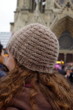 a woman with long red hair wearing a knitted hat in front of a cathedral