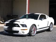 a white ford mustang parked in front of a building with red and black stripes on it