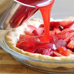 someone pouring syrup onto a pie with strawberries in it