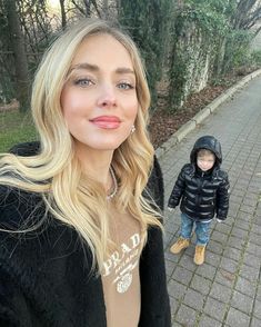 a woman standing next to a little boy on a brick walkway with trees in the background