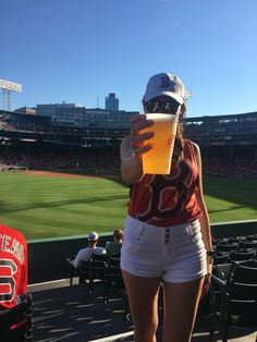 a woman is holding a drink at a baseball game