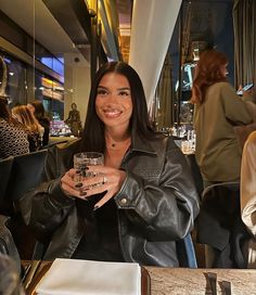 a woman sitting at a table with a glass in her hand and smiling for the camera