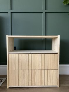 a wooden cabinet sitting on top of a hard wood floor next to a green wall