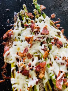 asparagus covered in bacon and cheese on a black surface