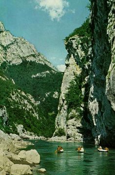 some people are swimming in the water near large rocks and mountains with green trees on either side