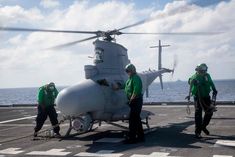 two men in green shirts standing next to a helicopter on the deck of an aircraft carrier