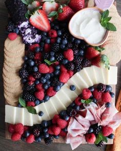 an assortment of cheeses, berries and crackers on a cutting board with dip