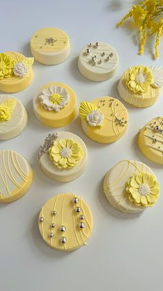 many yellow and white decorated cakes are arranged on a table with some flowers in the middle