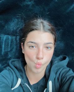 a woman sticking her tongue out while laying on a blue velvet couch in front of the camera