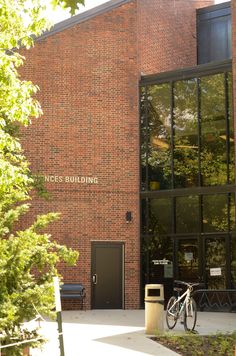 a bike is parked in front of a brick building with glass doors and trees around it