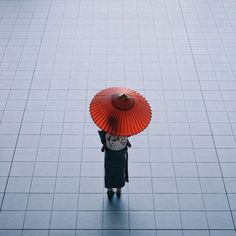 a person with an umbrella walking on a tile floor in front of a building, looking down at the ground