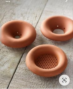 three brown ceramic bowls sitting on top of a wooden table next to each other with holes in them