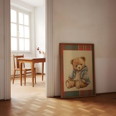 a teddy bear sitting on top of a wooden floor next to a table and chairs