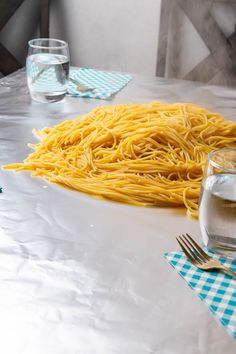 a table topped with lots of pasta next to two glasses of water and silverware