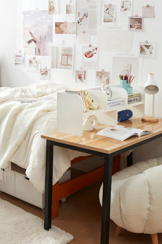 a desk with a laptop on it in front of a bed covered in white sheets