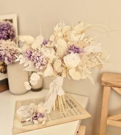 a bouquet of flowers sitting on top of a table next to a vase filled with purple and white flowers