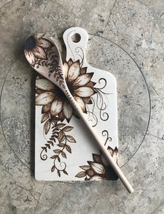 two spoons sitting on top of a cutting board with flowers painted on the side