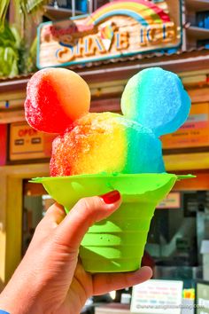 someone holding up a mickey mouse ice cream cone in front of a disney world store