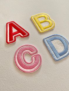 three different types of embroidered letters on a white shirt with red, blue and yellow stitching