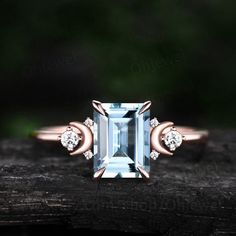 an aqua blue topazte and diamond ring on a piece of wood with green leaves in the background