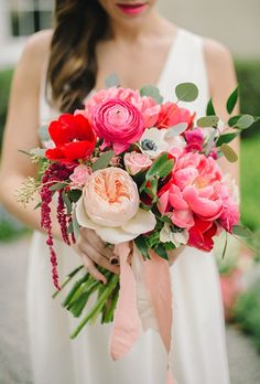 a woman in white dress holding a pink and red bouquet with greenery on it