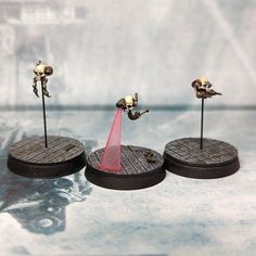 three small metal figurines on wooden bases with red liquid pouring out of them