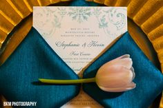 a tulip on top of a blue napkin next to a white and gold wedding card