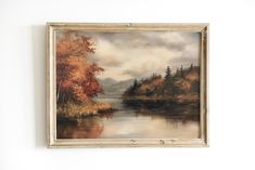 a painting hanging on the wall next to a white wall with a lake and trees