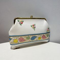 Vintage 60s White Vinyl Floral Embroidered Kiss Lock Clutch/Purse, Cosmetics Bag. This Purse Was Never Used. White Vinyl With Embroidered Floral,Pink, Blue, Yellow, Green And Red, On Front. Floral Embroidered Ribbon With Gold Accents Along Bottom Front. Deep Zippered Compartment On Bottom. Green, And Tan Floral Lined. Interior Is Lined With Green Vinyl. Gold Tone Frame And Kiss Lock. Tag From Sale Left A Tiny Hole On Side Front, Gold Tone Frame Has Some Fading (See Pics) Otherwise, No Flaws, Cle Vintage White Rectangular Bag, Vintage White Handheld Shoulder Bag, White Vintage Rectangular Bag, White Rectangular Vintage Bag, Retro Pouch Clutch For Daily Use, Compact White Bag For Daily Use, Vintage White Pouch Shoulder Bag, Embroidered Cream Rectangular Clutch, Vintage White Clutch For Everyday Use