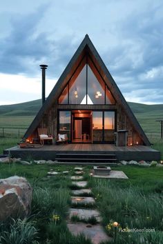 a - frame cabin in the middle of a grassy field at dusk with steps leading up to it