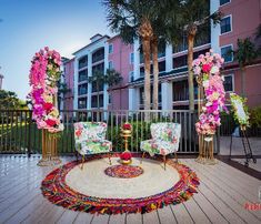 an outdoor area with chairs, rugs and flowers on the ground in front of palm trees