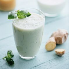 a glass filled with green smoothie next to sliced ginger on a blue counter top