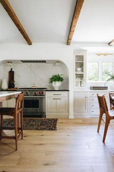 a kitchen with white cabinets and an oven in the center, surrounded by wooden chairs