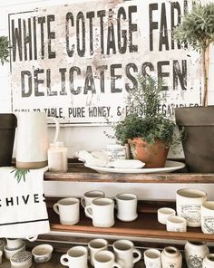 coffee cups and mugs are on display in front of a sign that says white cottage farm delicatessen