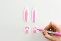 a person is drawing pink bunny ears on a white surface with a marker and pen