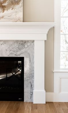 an empty room with a white fireplace and wood floors in front of a painting on the wall