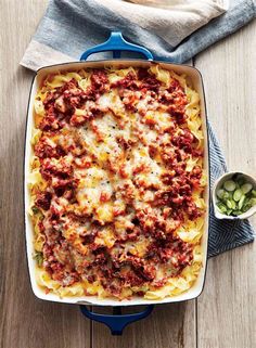 a blue casserole dish filled with pasta, meat and sauces on a wooden table