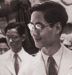 a man in suit and tie standing next to another man with glasses on his face