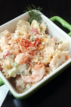 a bowl filled with pasta and shrimp on top of a green handled spatula next to a white napkin