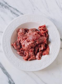 a white bowl filled with meat on top of a marble counter